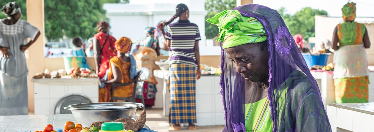 Local produce sold at the market includes items such as: legumes, root vegetables, tomatoes, garlic and onions. Here, Mme Maty Mbaye waits for a client while she cuts green onions. 