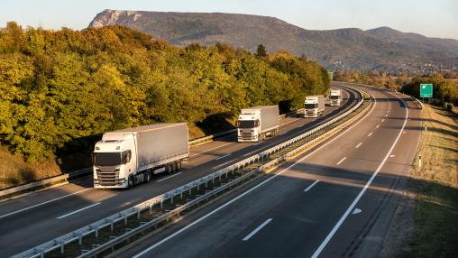Convoy or caravan of transportation trucks passing on a highway at sunset. Highway transit transportation with red and yellow lorry trucks